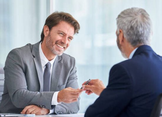Smiling mature businessman giving pen to his partner in office